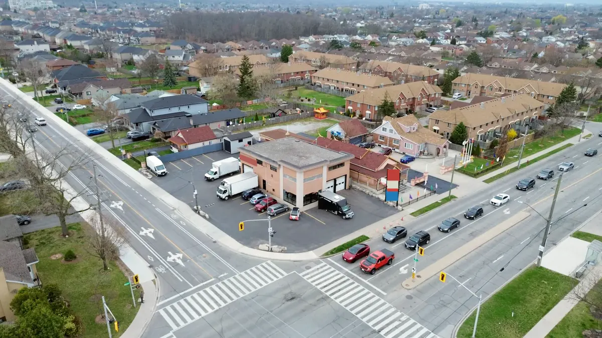 Aerial view of the corner of Barton Street and Dewitt Road: the two-storey building, its lot, and cars queued at the signal